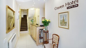 A hotel corridor with a staircase, a reception desk, and a framed picture on the wall. - The Craven Hotel (London)