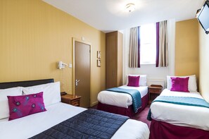 Camera d'albergo con tre letti, un'armadio in legno, un comodino e una TV a parete, oltre a una finestra con tende.