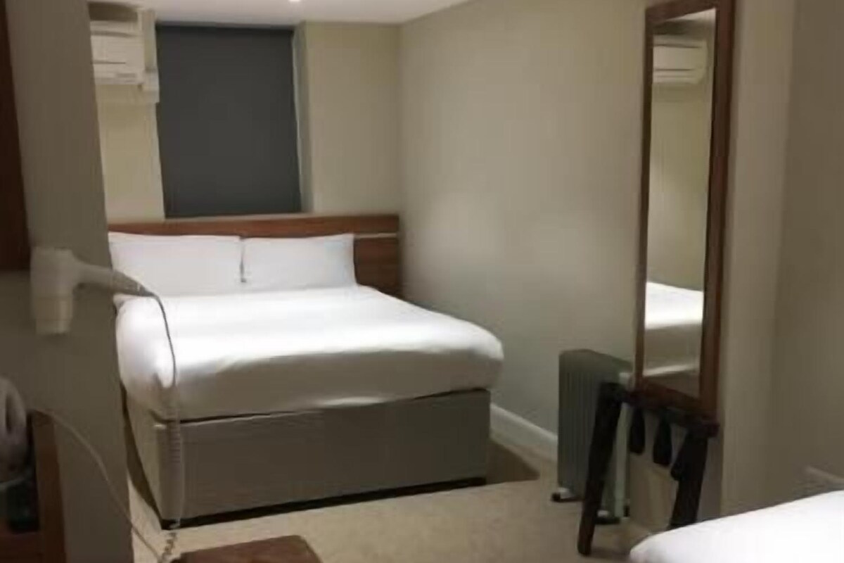 A hotel room with a bed, a desk, a chair, a mirror, and a radiator.