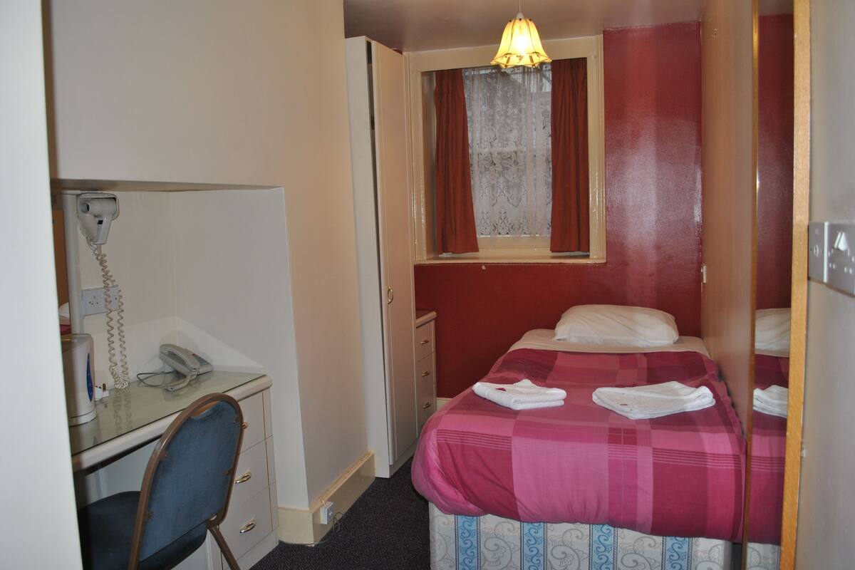 A hotel room with a desk, chair, bed, and a window with curtains.