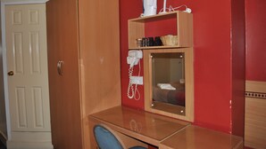 A room with a wooden wardrobe, a desk with a chair, a mirror, a hairdryer, and a shelf with a kettle and other items. - Grenville Hotel (London)