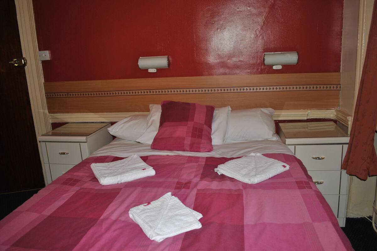 A hotel room with a bed, two bedside tables, a nightstand, and a red wall.