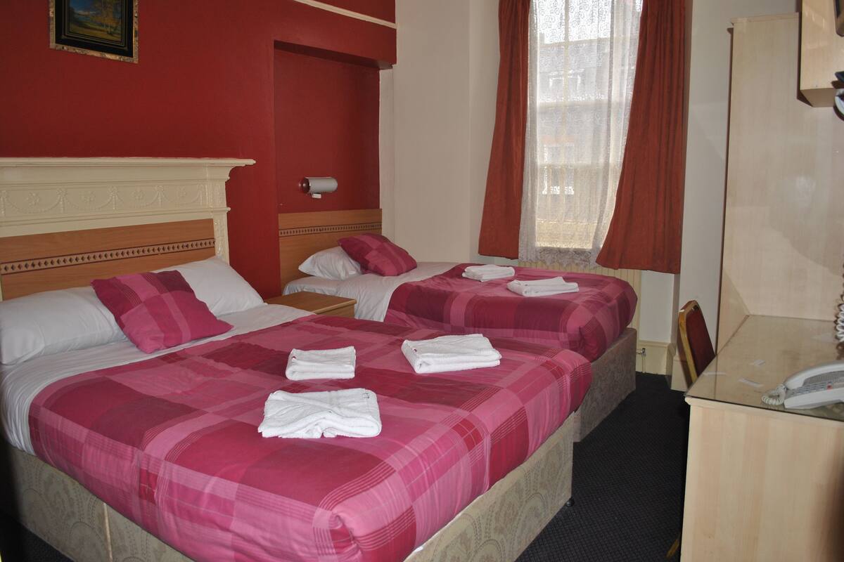 A hotel room with two beds, each with pink bedding and white pillows, and a wooden headboard. There is a wooden nightstand with a lamp and a telephone on it.