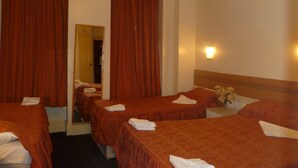 A hotel room with two beds, each with a red bedspread and white towels. There is a nightstand with a vase of flowers and a wall-mounted light. - Grenville Hotel (London)