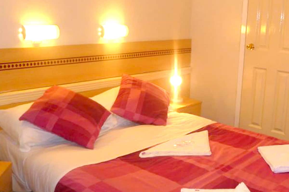 Une chambre d’hôtel avec un lit, deux oreillers, une table de chevet et une lampe de chevet.