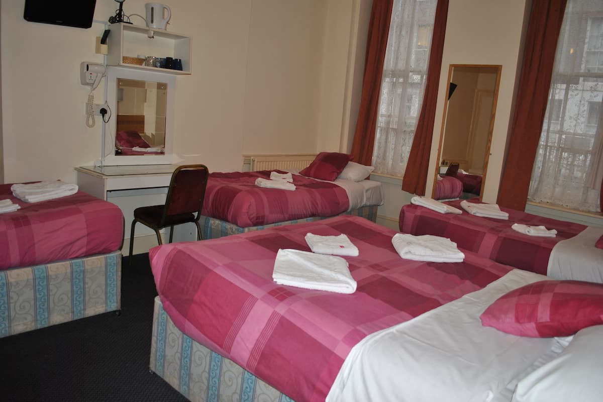 Une chambre d’hôtel avec trois lits, chacun agrémenté de draps roses et de serviettes blanches. On y trouve un bureau avec un miroir, une chaise et un téléphone.