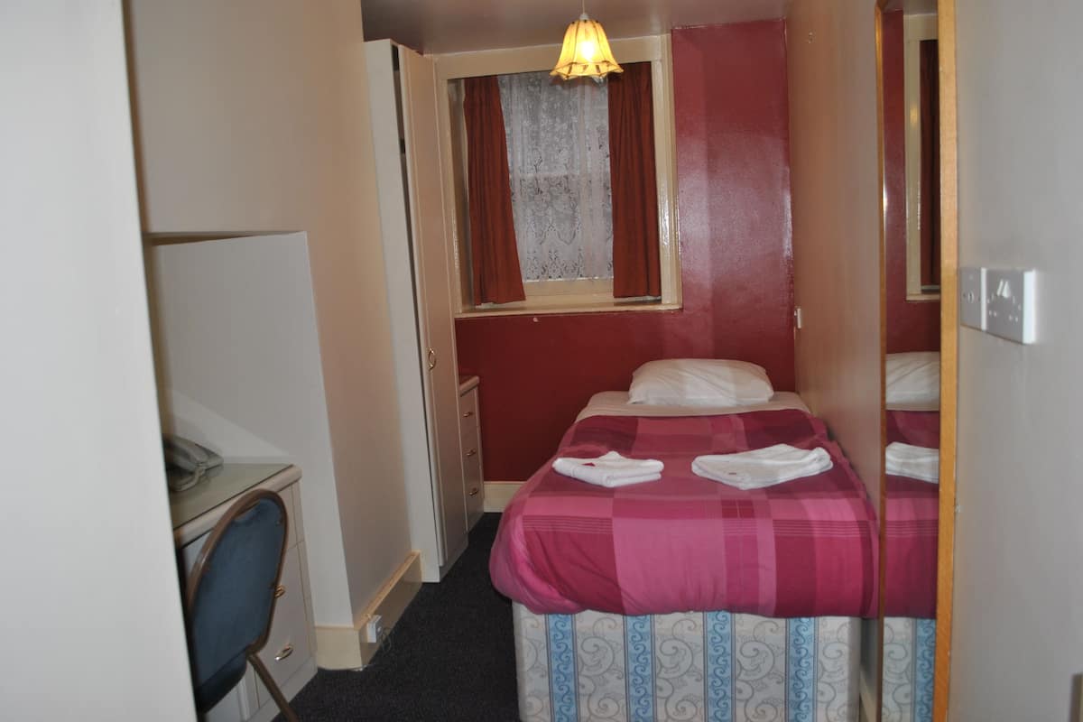 Une chambre d’hôtel de taille réduite, comprenant un lit simple, un bureau et une chaise.