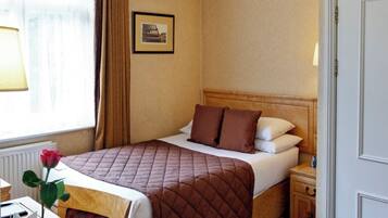 A hotel room with a bed, bedside table, lamp, and a window with curtains.
