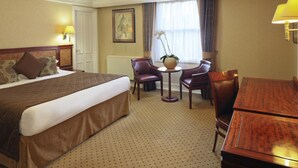 Ein Hotelzimmer mit einem großen Bett, einem kleinen Tisch mit Stühlen, einem Schreibtisch und einem Fenster mit Vorhängen.