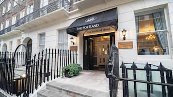 The entrance to The Portland Hotel, featuring a black awning, a signboard with the hotel's name, and a staircase leading to the entrance.