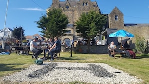 Un espace extérieur aménagé avec des tables et des bancs en pierre, un chemin de gravier et, en arrière-plan, un bâtiment historique.