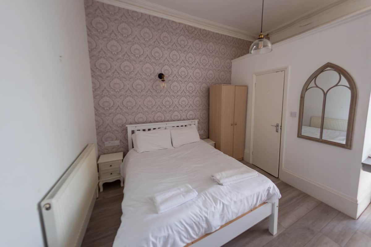 Une chambre à coucher comprenant un lit, une armoire, une table de chevet, un miroir et un papier peint à motifs.