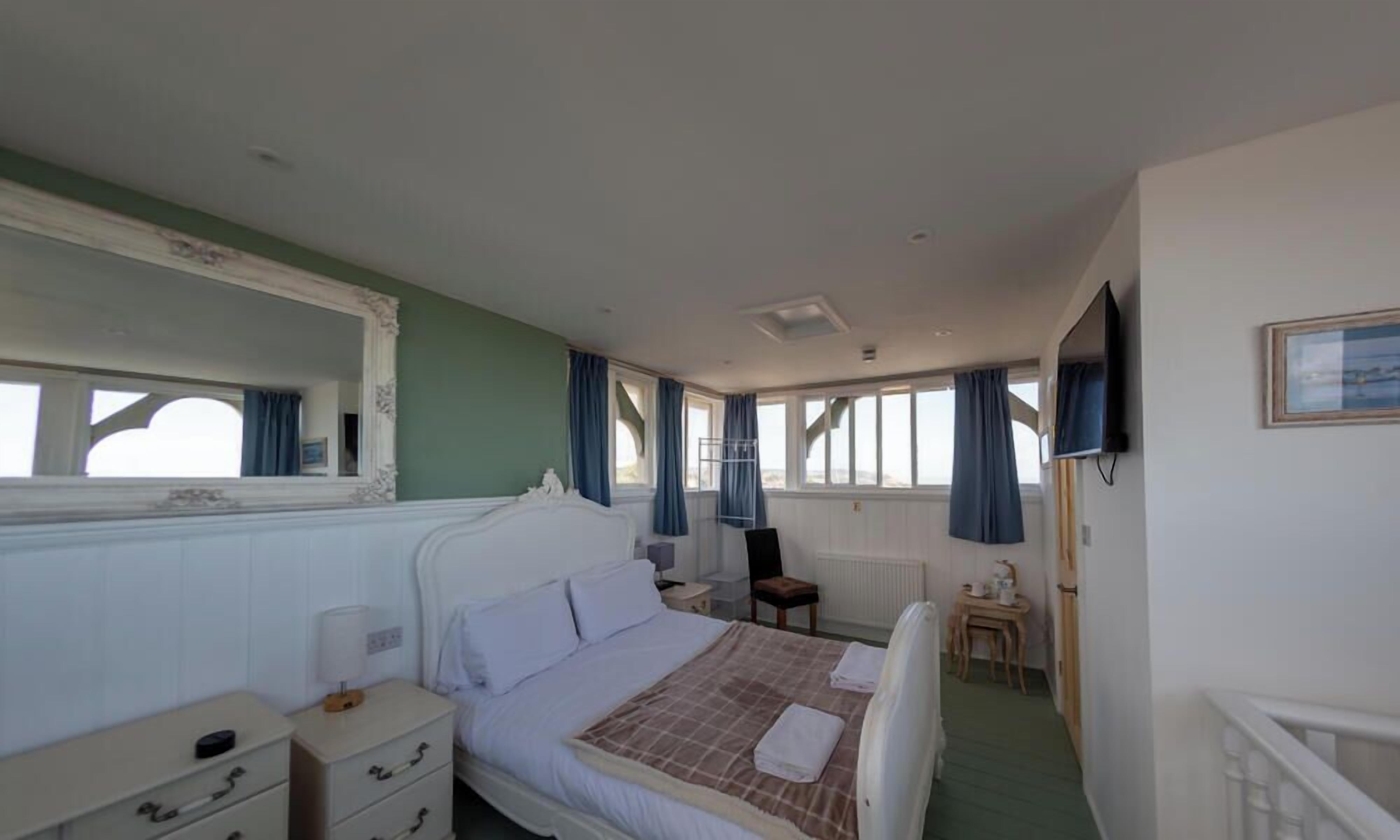Habitación de hotel con cama, una silla, una mesita, televisión y ventana con cortinas.