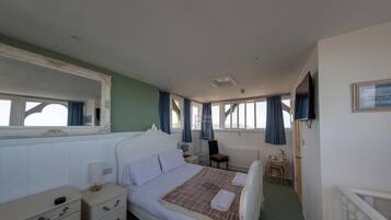 Habitación de hotel con cama, una silla, una mesita, televisión y ventana con cortinas.