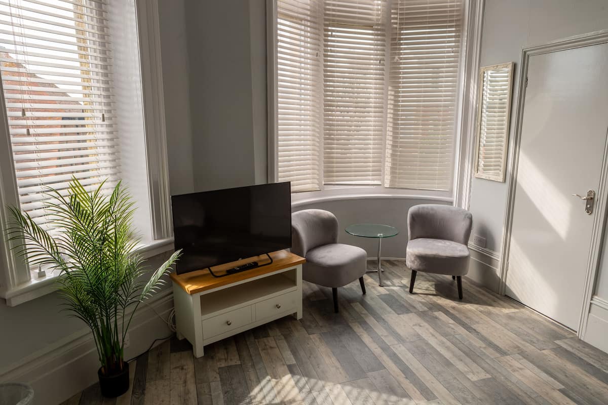 Un salon moderne avec un téléviseur à écran plat, deux fauteuils, une table basse en verre et une plante en pot.