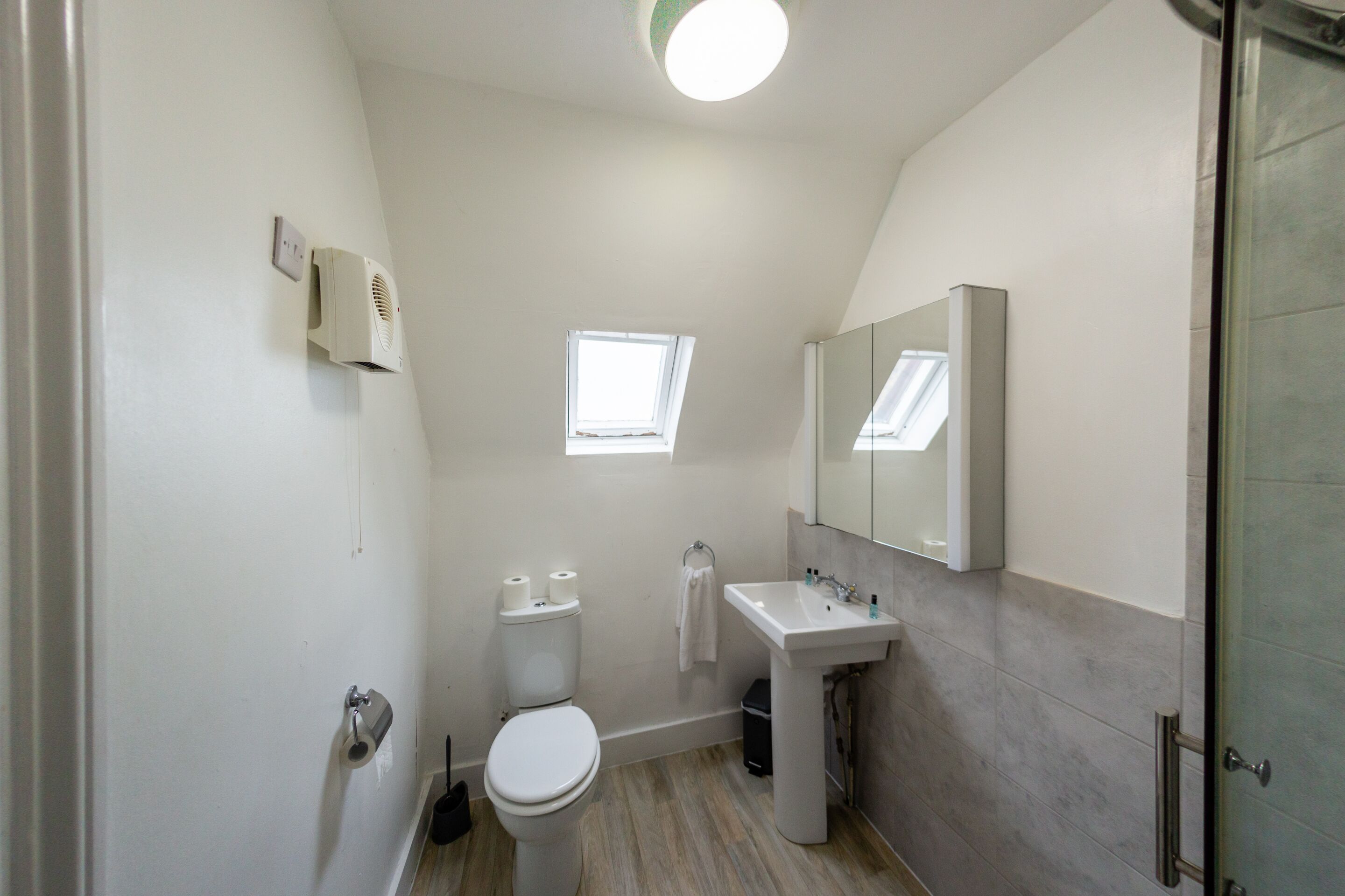 A bathroom with a toilet, sink, mirror, and a small window.