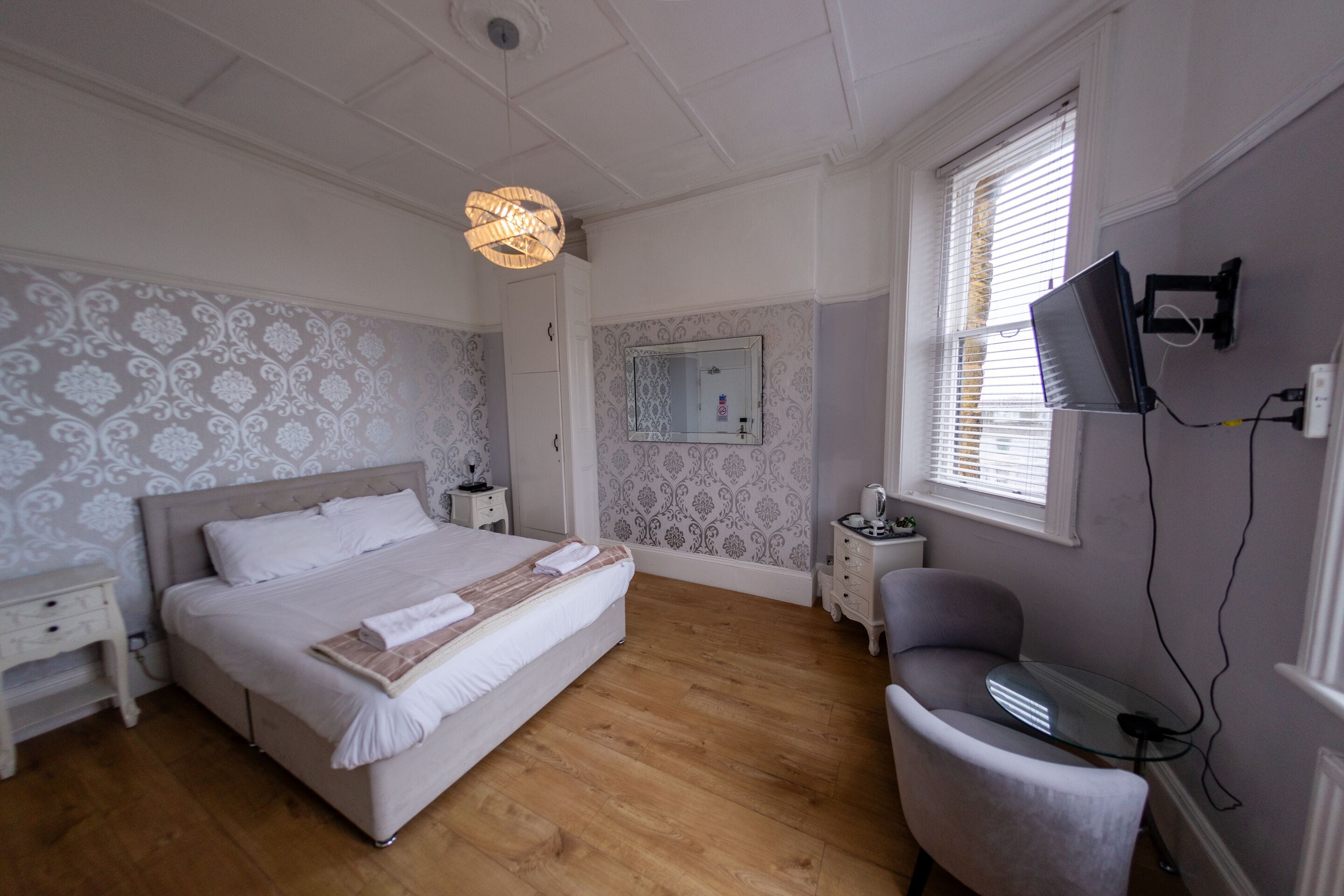 A bedroom with a bed, bedside tables, a chair, a TV, and a window with blinds.