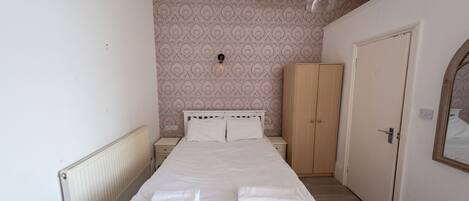 A bedroom with a bed, a wardrobe, a door, and a radiator.