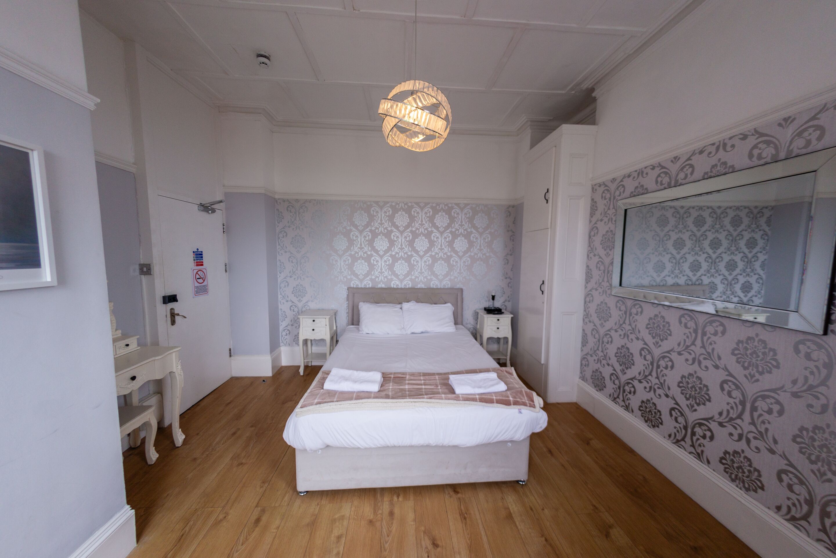 A bedroom with a bed, bedside tables, a wardrobe, a mirror, and a chandelier.