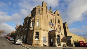 Un bâtiment historique en pierre, doté d’une tour d’angle imposante, d’une grande entrée en arc de cercle et d’une enseigne indiquant qu’il s’agit d’un pub.