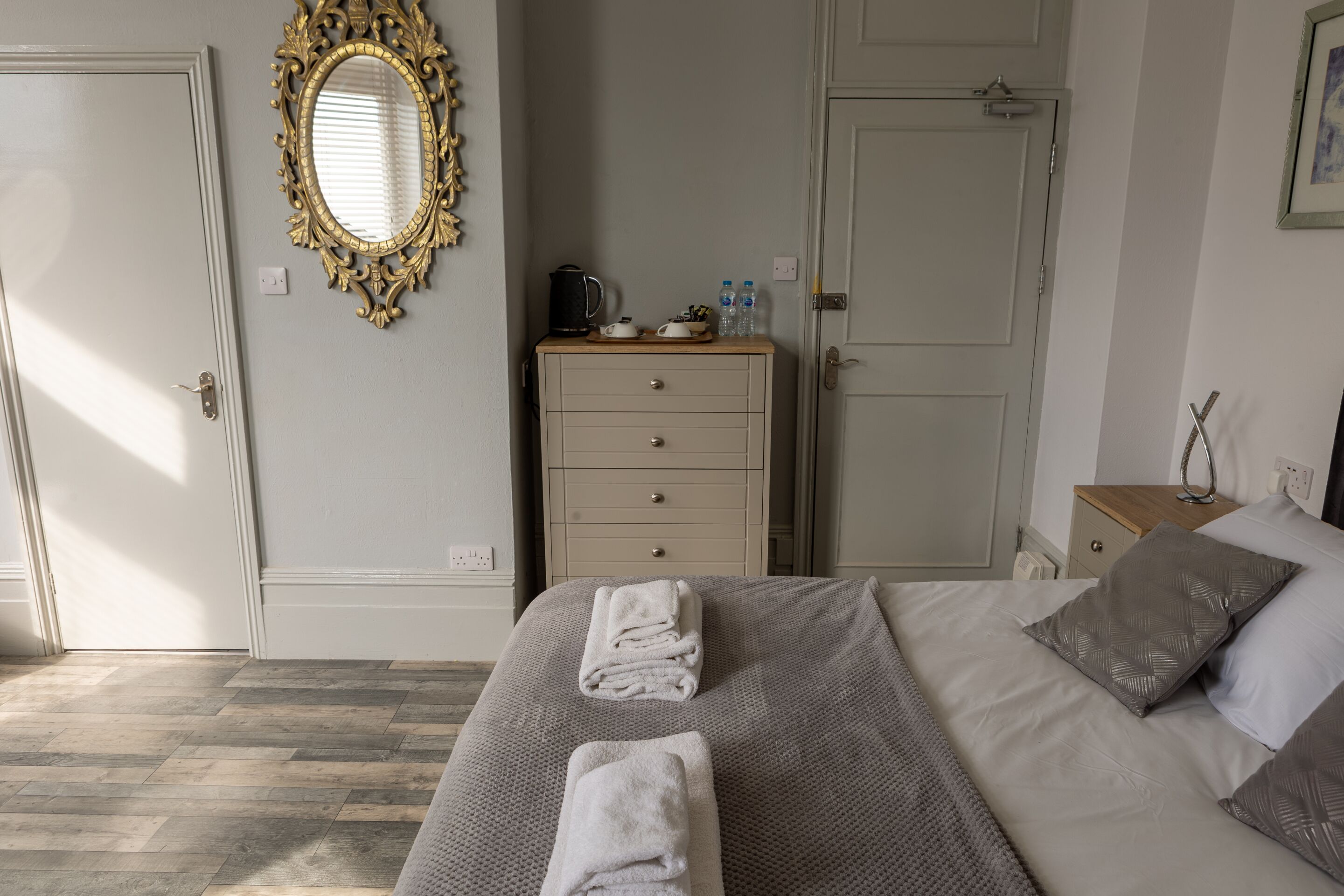 Un dormitorio ordenado con cama, cómoda, espejo y mesita de noche.
