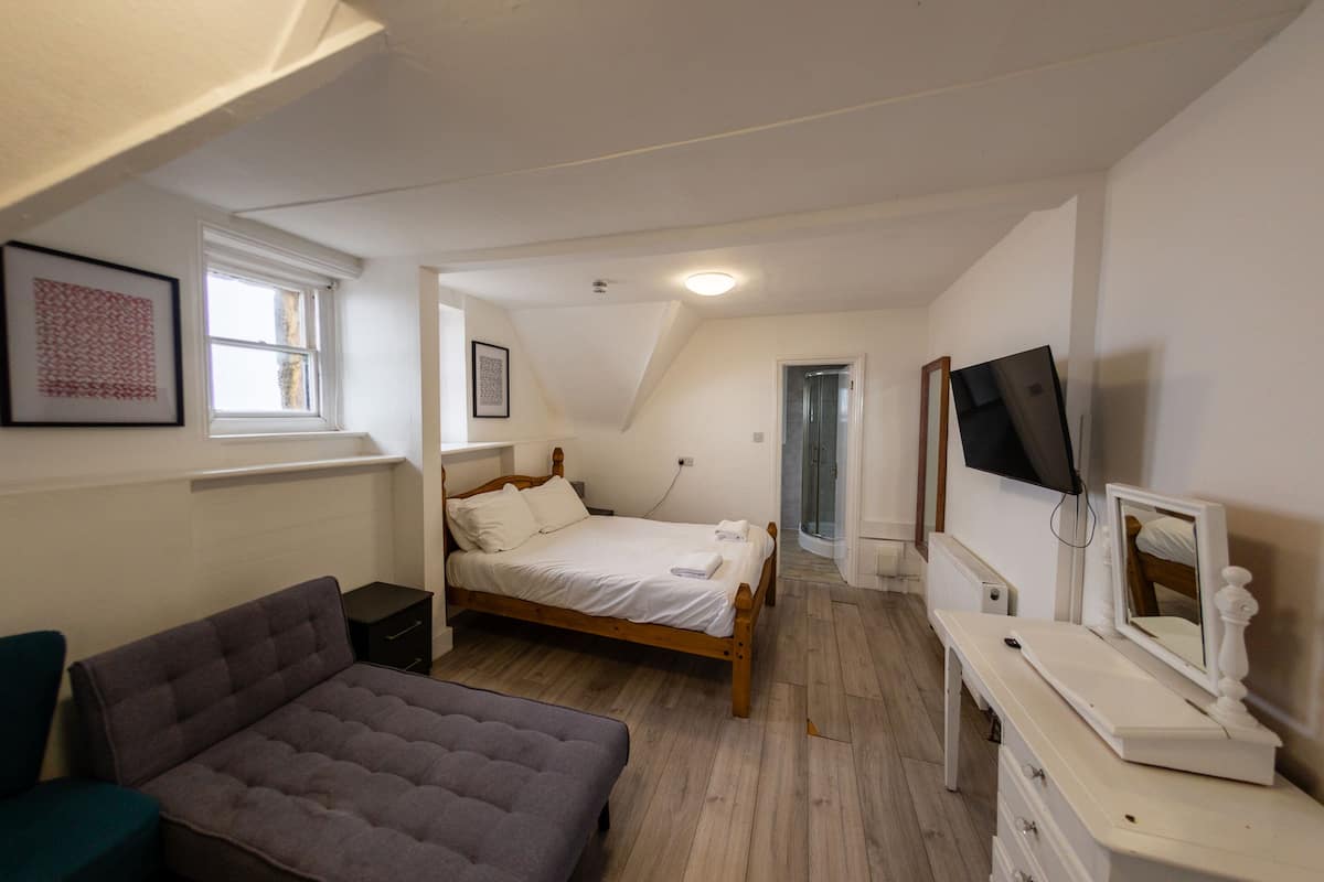Une chambre à coucher avec un lit, une table de chevet, une commode, un téléviseur et une fenêtre.