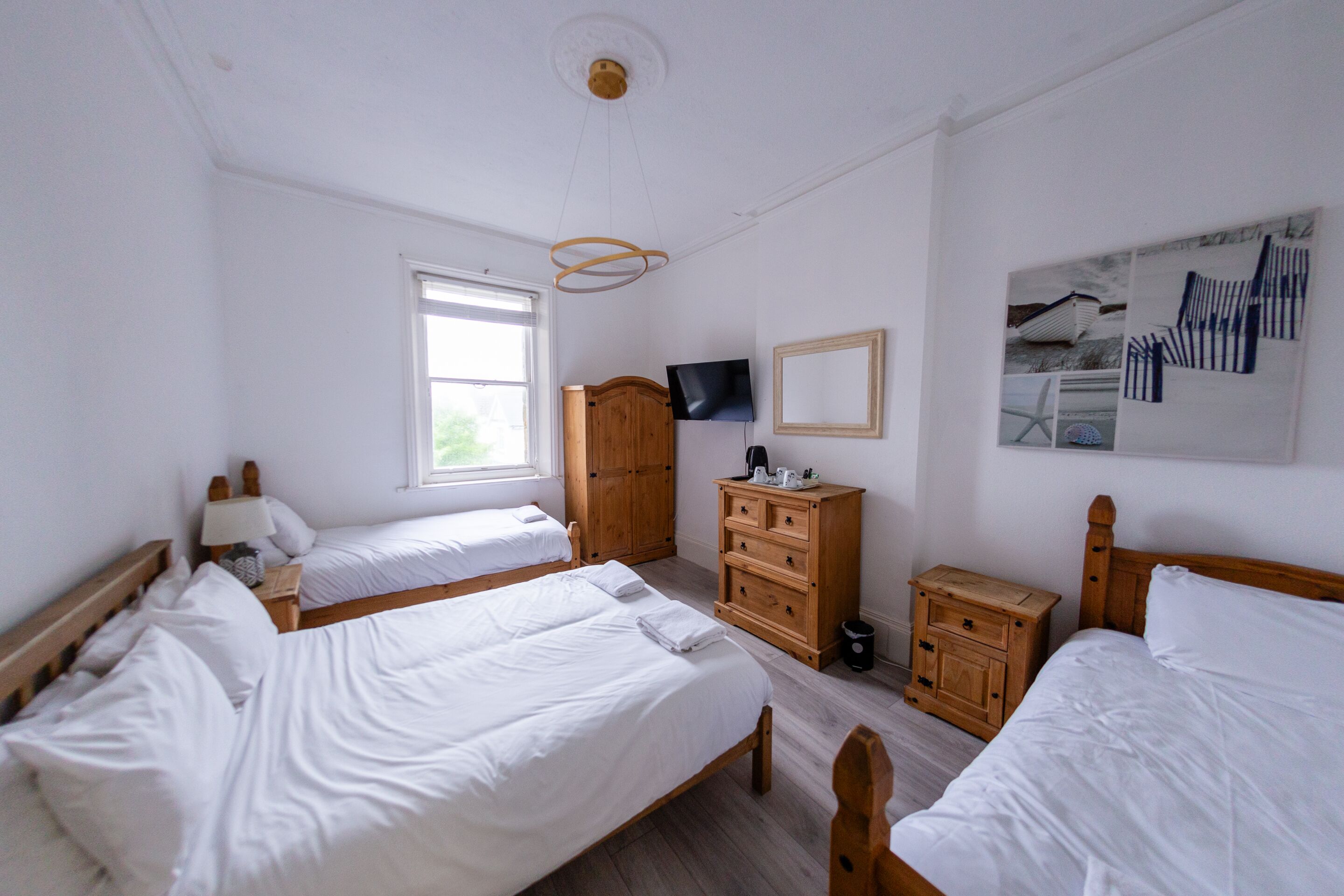 Een kamer met twee bedden, een houten garderobe, een televisie en een raam.