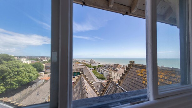 Une vue panoramique d’une ville côtière, prise depuis un point d’observation élevé, comprenant des bâtiments, une vue sur la mer et un ciel dégagé.