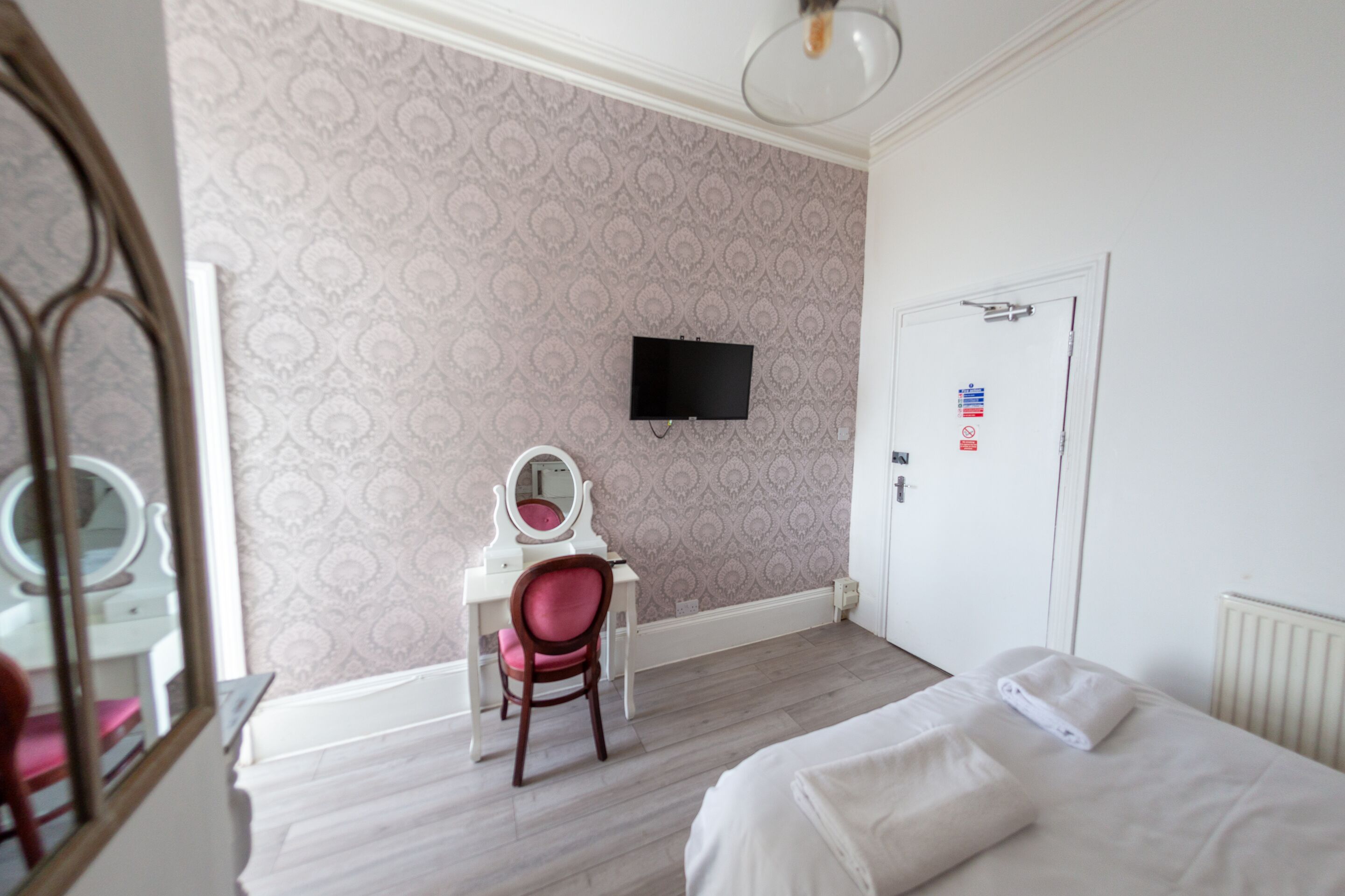 Habitación de hotel con cama, escritorio con silla, televisión y puerta con un cartel.