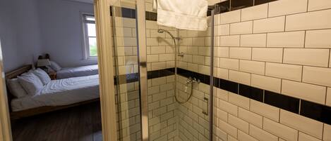 Un bagno con doccia vetrata, pareti piastrellate di bianco e un letto nella stanza adiacente.