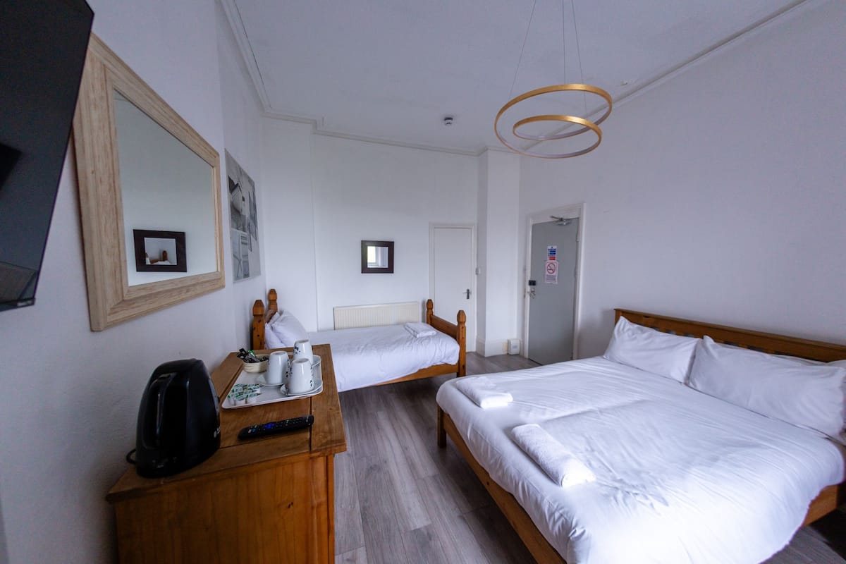 Une chambre d’hôtel avec deux lits, une commode en bois, un miroir et un luminaire au plafond.