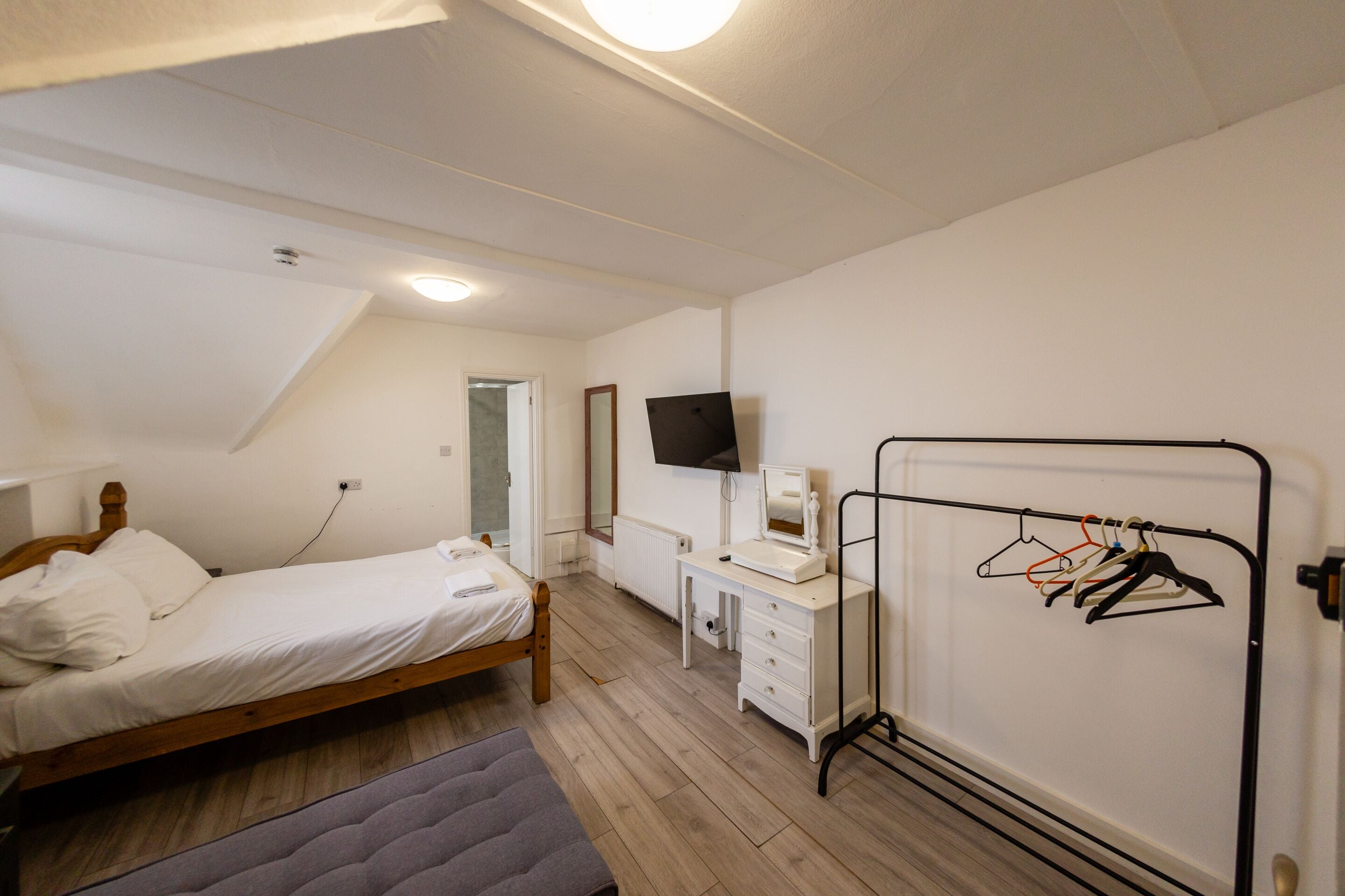 Una camera da letto con un letto, una cassettiera, una TV e un termosifone con appendiabiti.