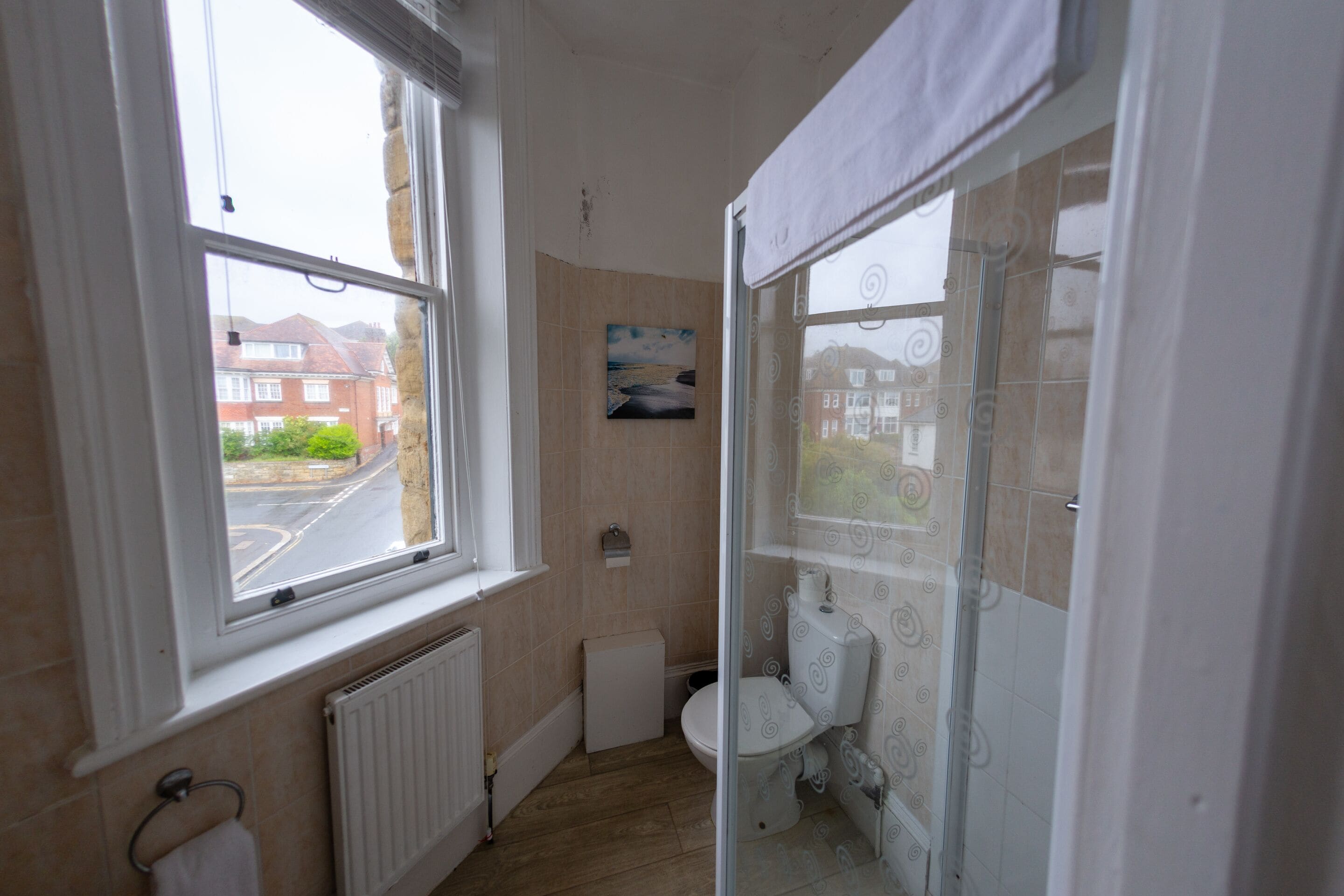 A bathroom with a toilet, a radiator, a window, and a shower.