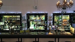 Un bar doté de trois étagères éclairées, remplies de bouteilles, d’un lustre et de tabourets de bar.