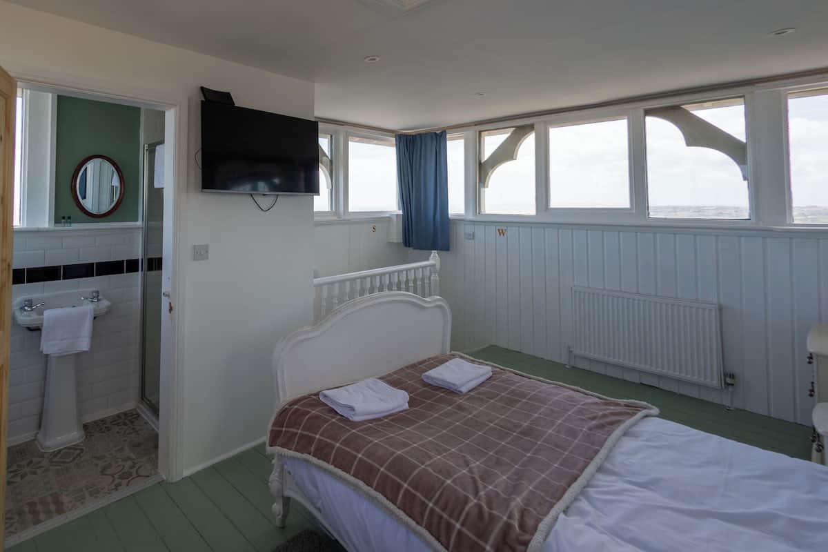 Une chambre à coucher comprenant un lit, un téléviseur, une fenêtre, un radiateur et une salle de bain avec un lavabo et un miroir.