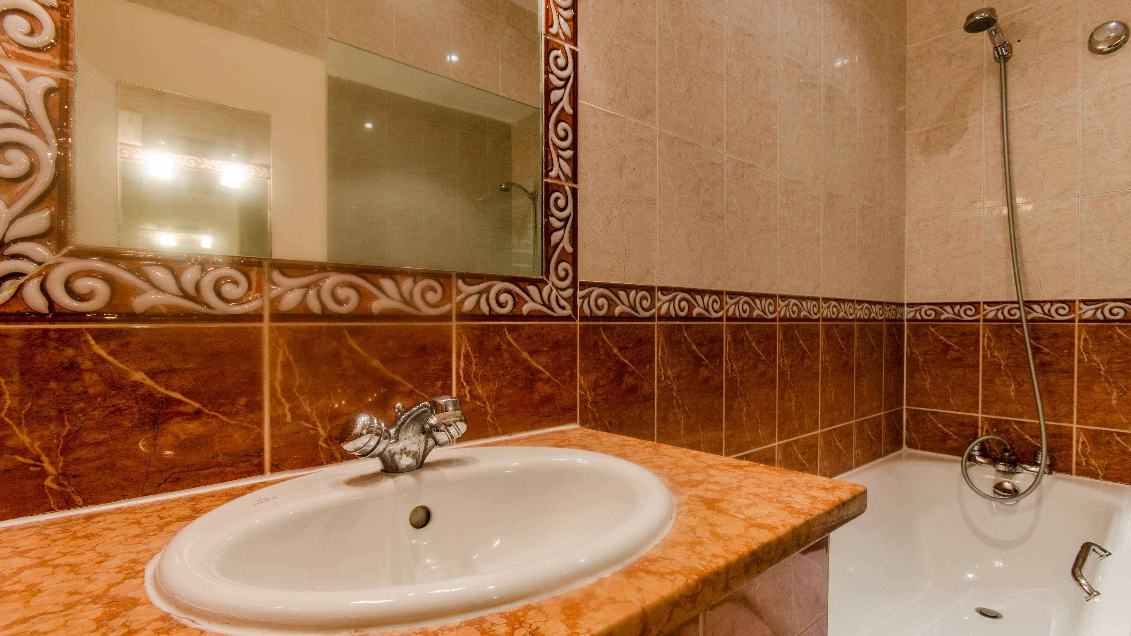 Ein Badezimmer mit Marmorwaschbecken und -badewanne, einem Spiegel und dekorativen Wandfliesen.