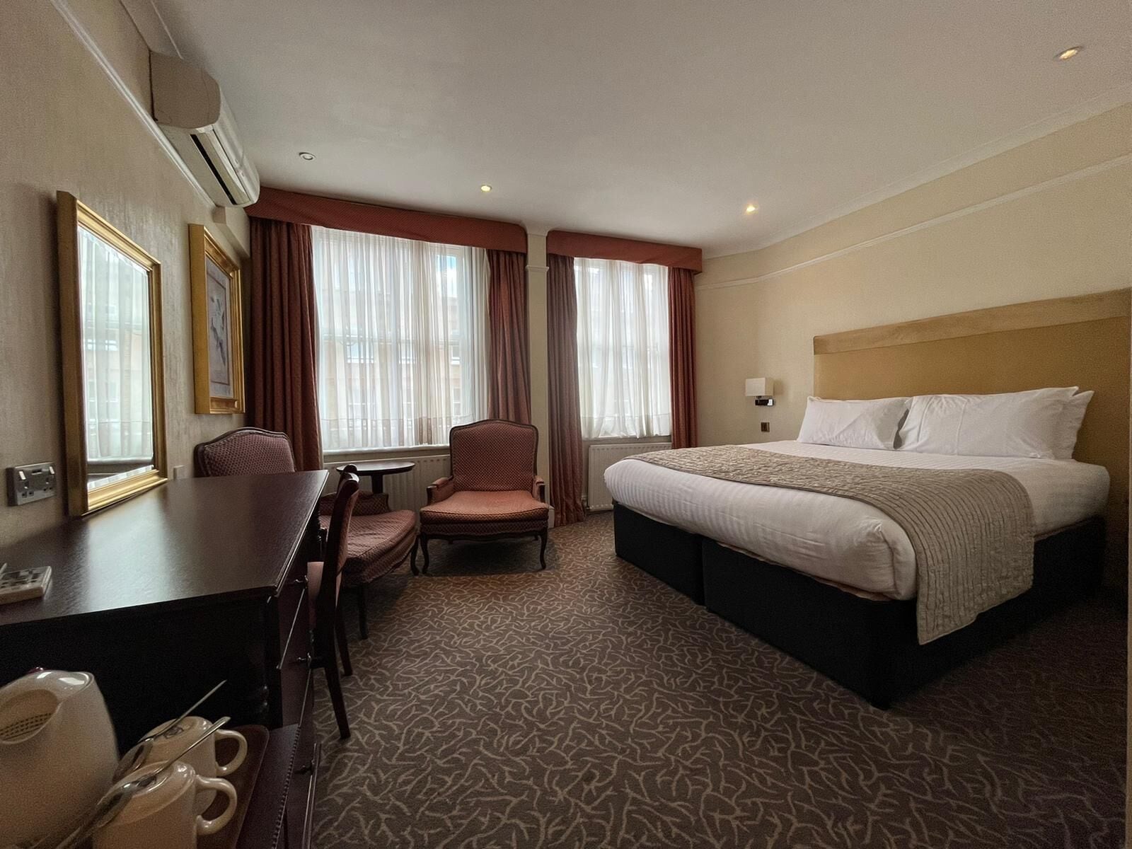 A hotel room with a bed, a desk, a chair, and a window with curtains.