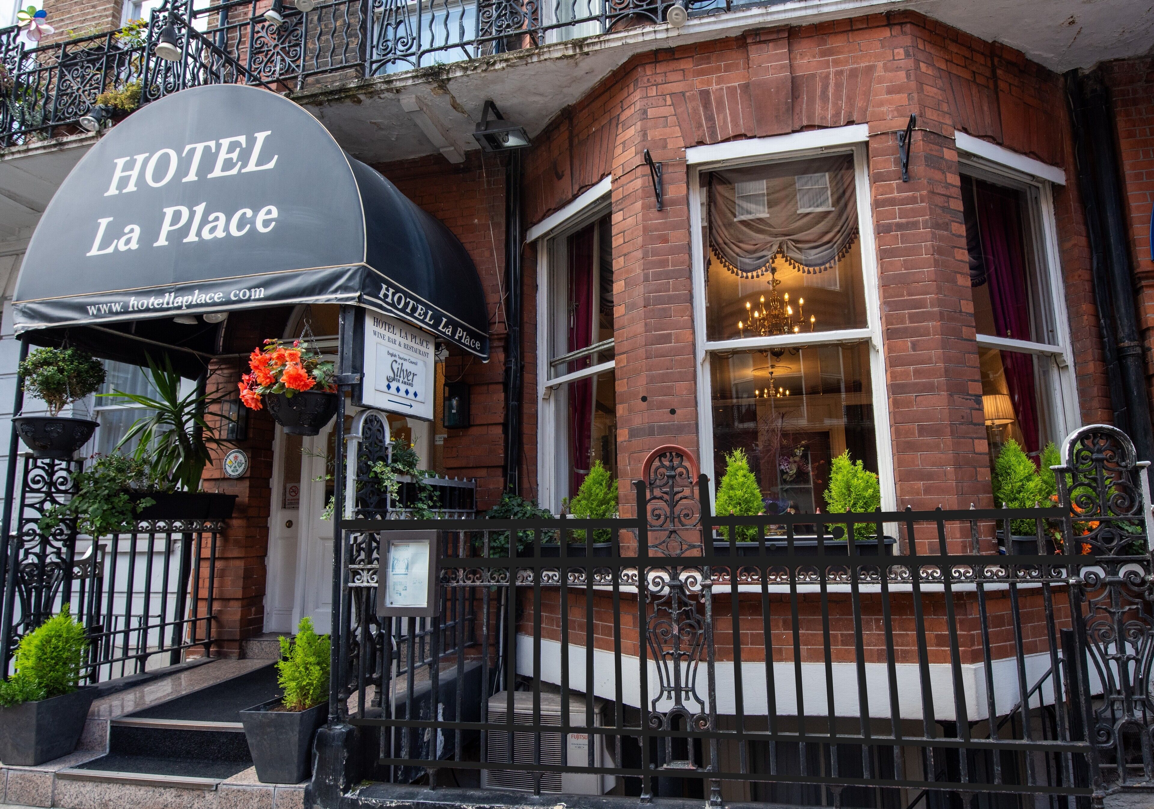 A hotel named HOTEL La Place with a black awning, brick facade, and a black wrought iron fence.