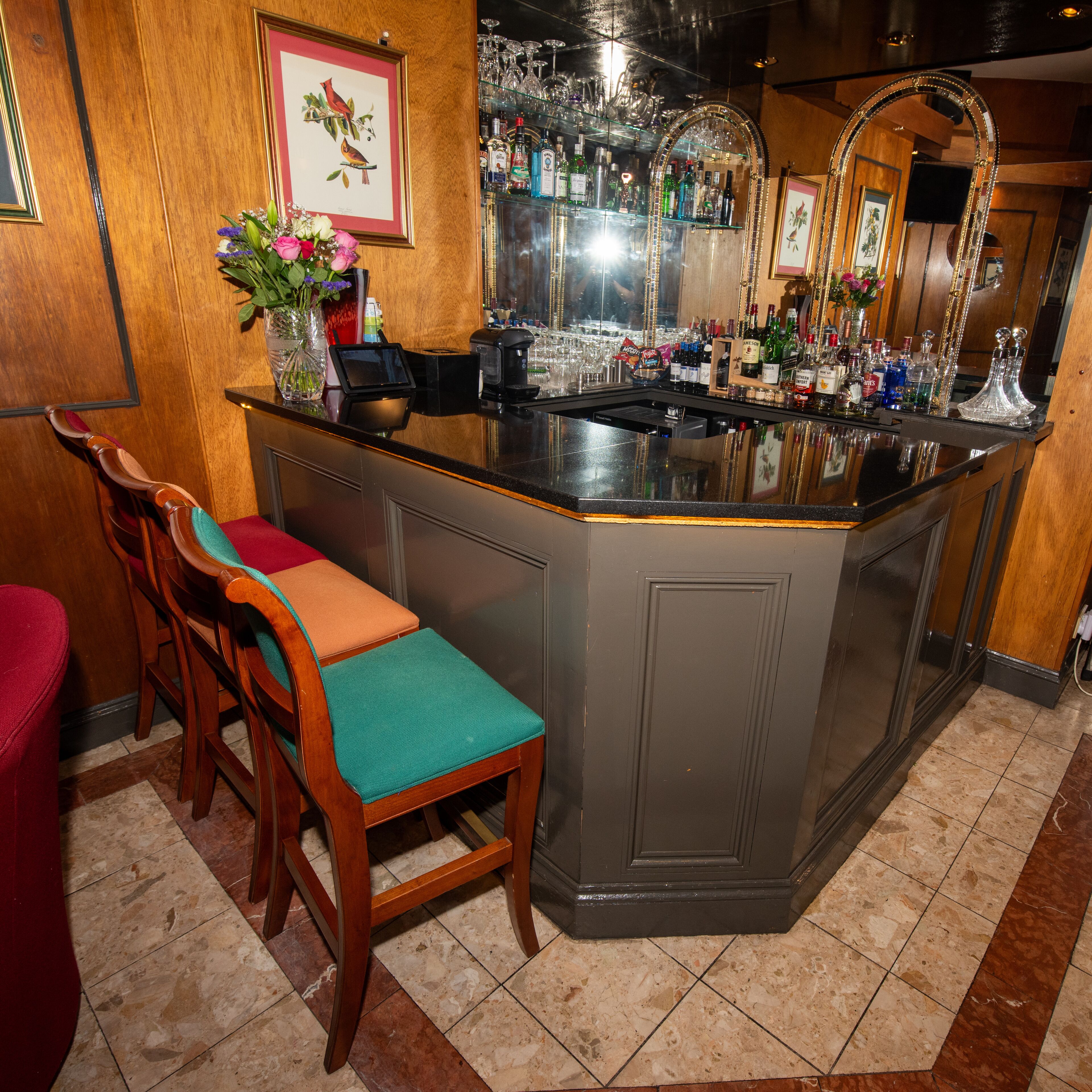 Un espace bar comprenant un comptoir, des tabourets de bar et une variété de bouteilles et de verres.