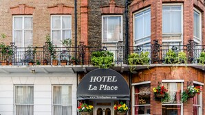 Hotel llamado "La Place" con un letrero negro, fachada de ladrillo y balcones con plantas en macetas.