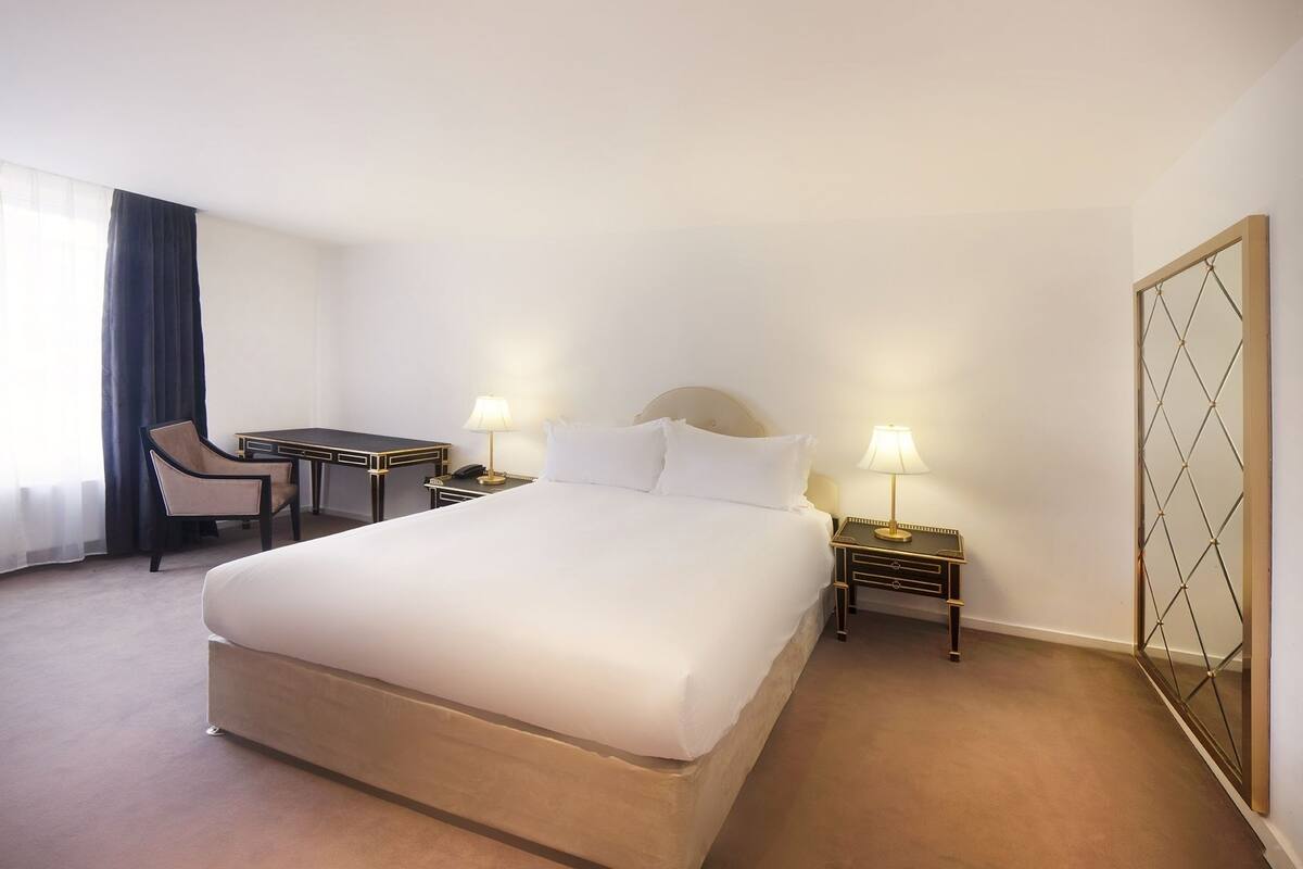 Una habitación de hotel con una cama grande, un escritorio, dos mesitas de noche, una silla y un armario.