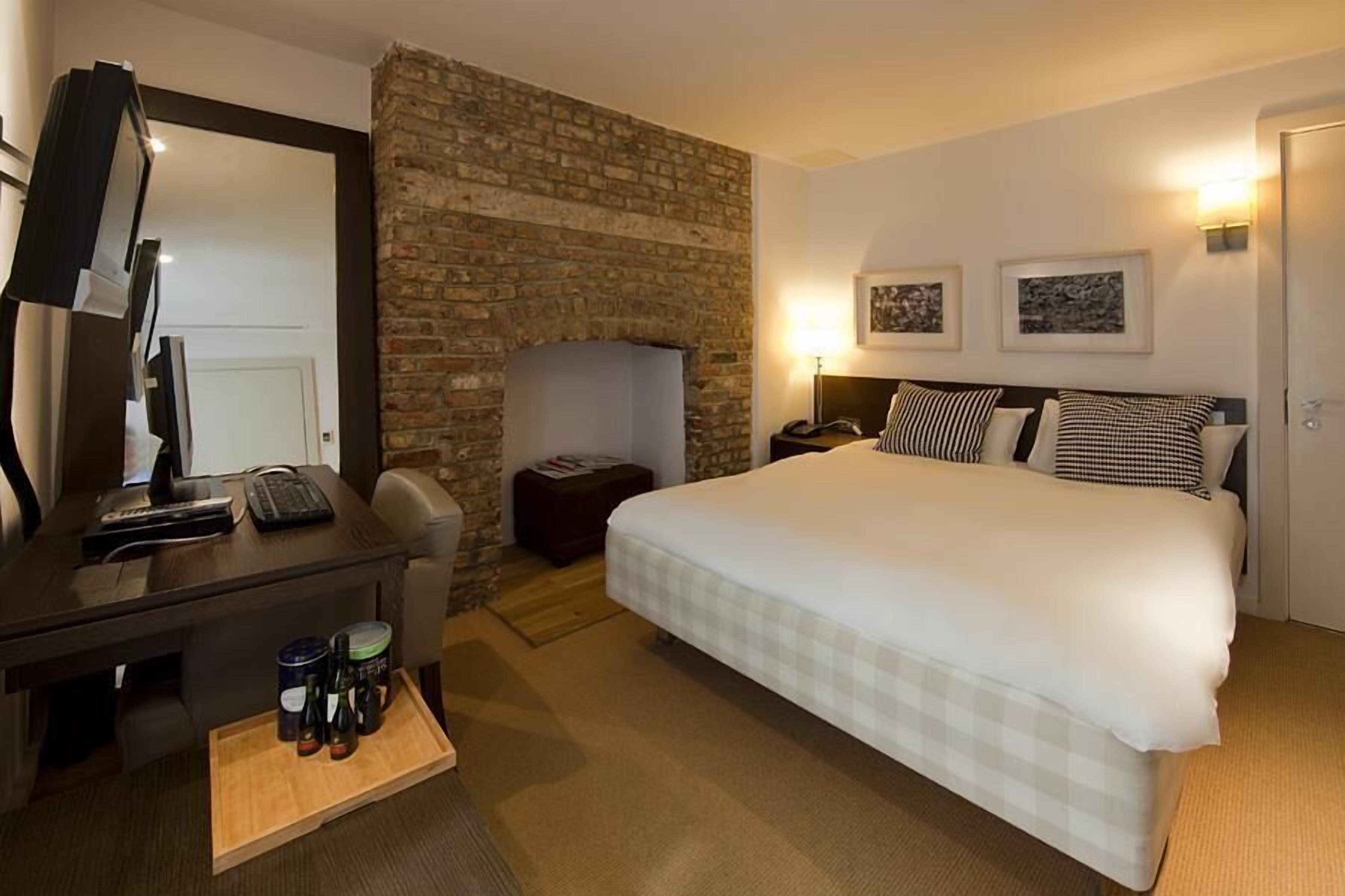 Habitación de hotel con una cama grande, un escritorio con ordenador, televisor y chimenea.