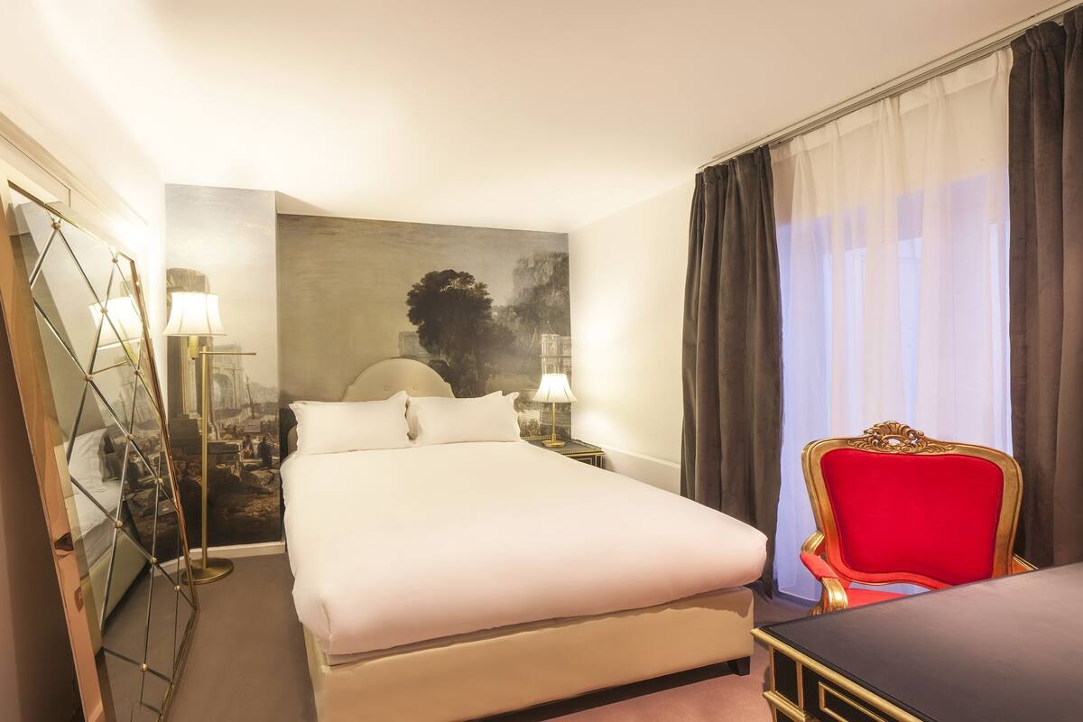 Una habitación de hotel con una cama grande, una silla roja, un escritorio y un espejo.