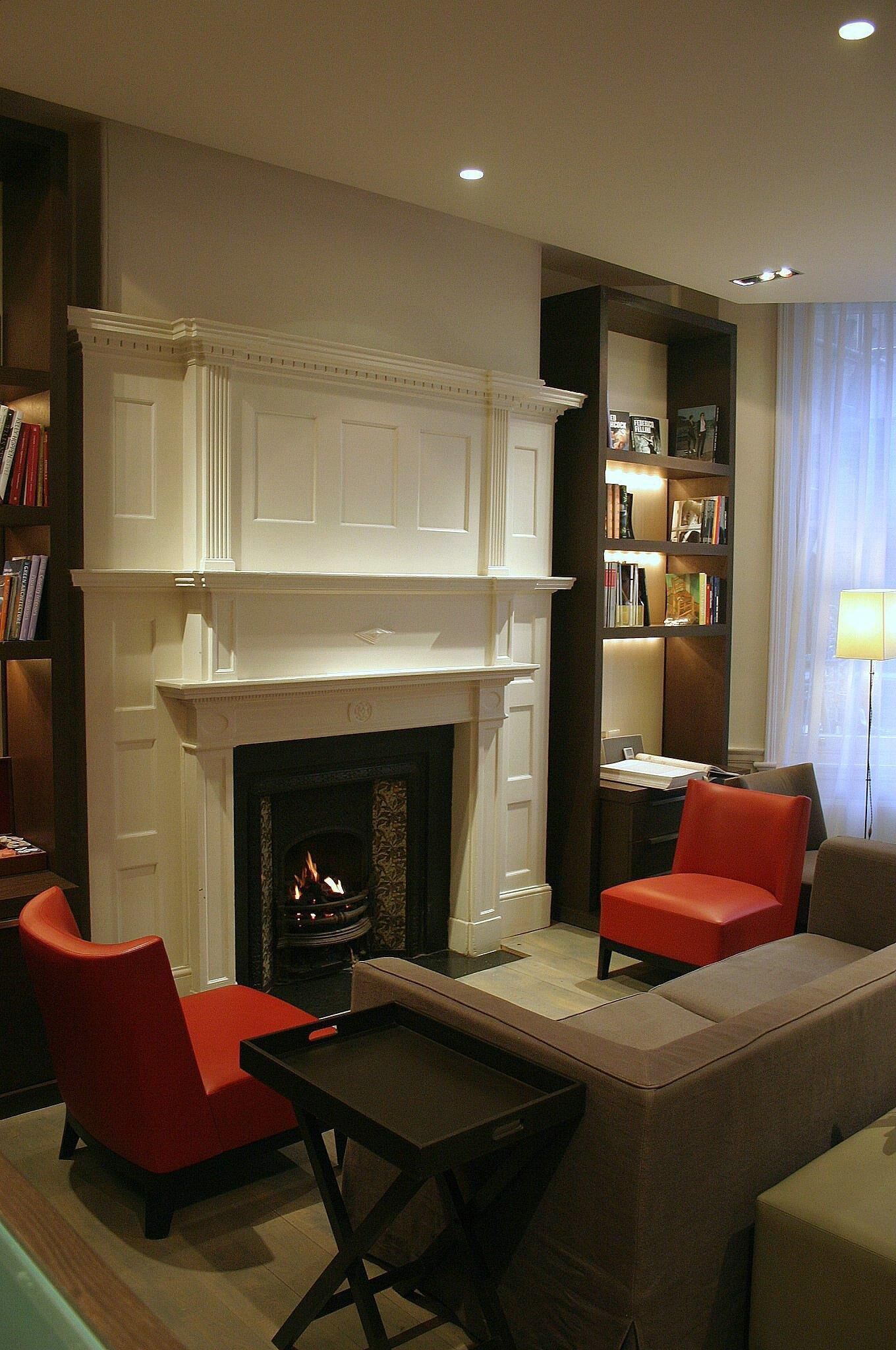 A living room with a fireplace, red chairs, a sofa, a small table, and bookshelves.