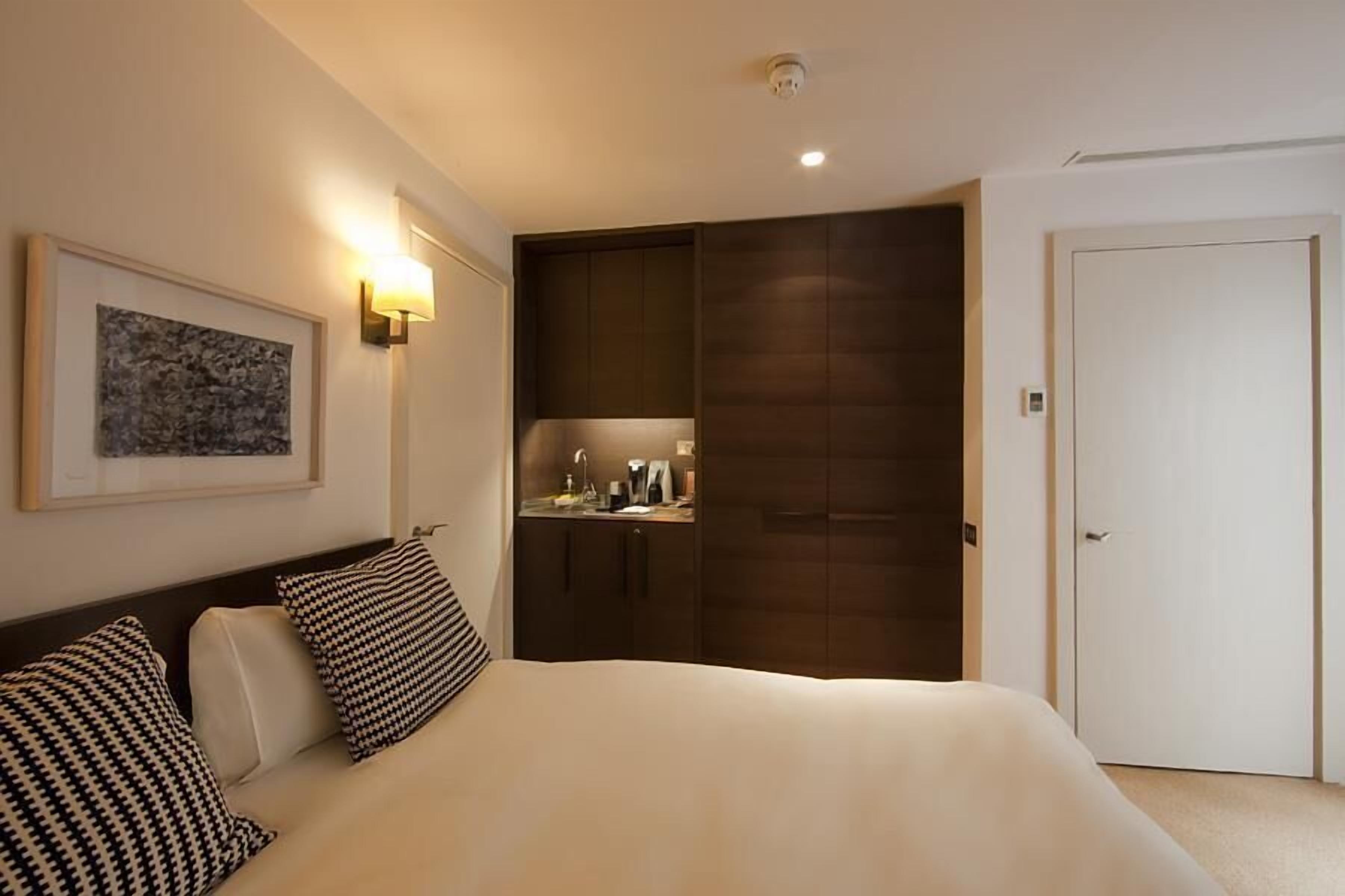 A hotel room with a bed, a bedside table, a wardrobe, and a framed picture on the wall.