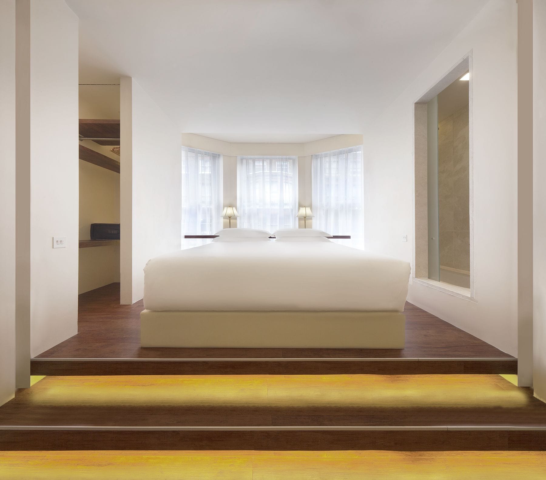 A modern hotel bedroom with a large bed, two bedside lamps, and a view of a tiled bathroom.
