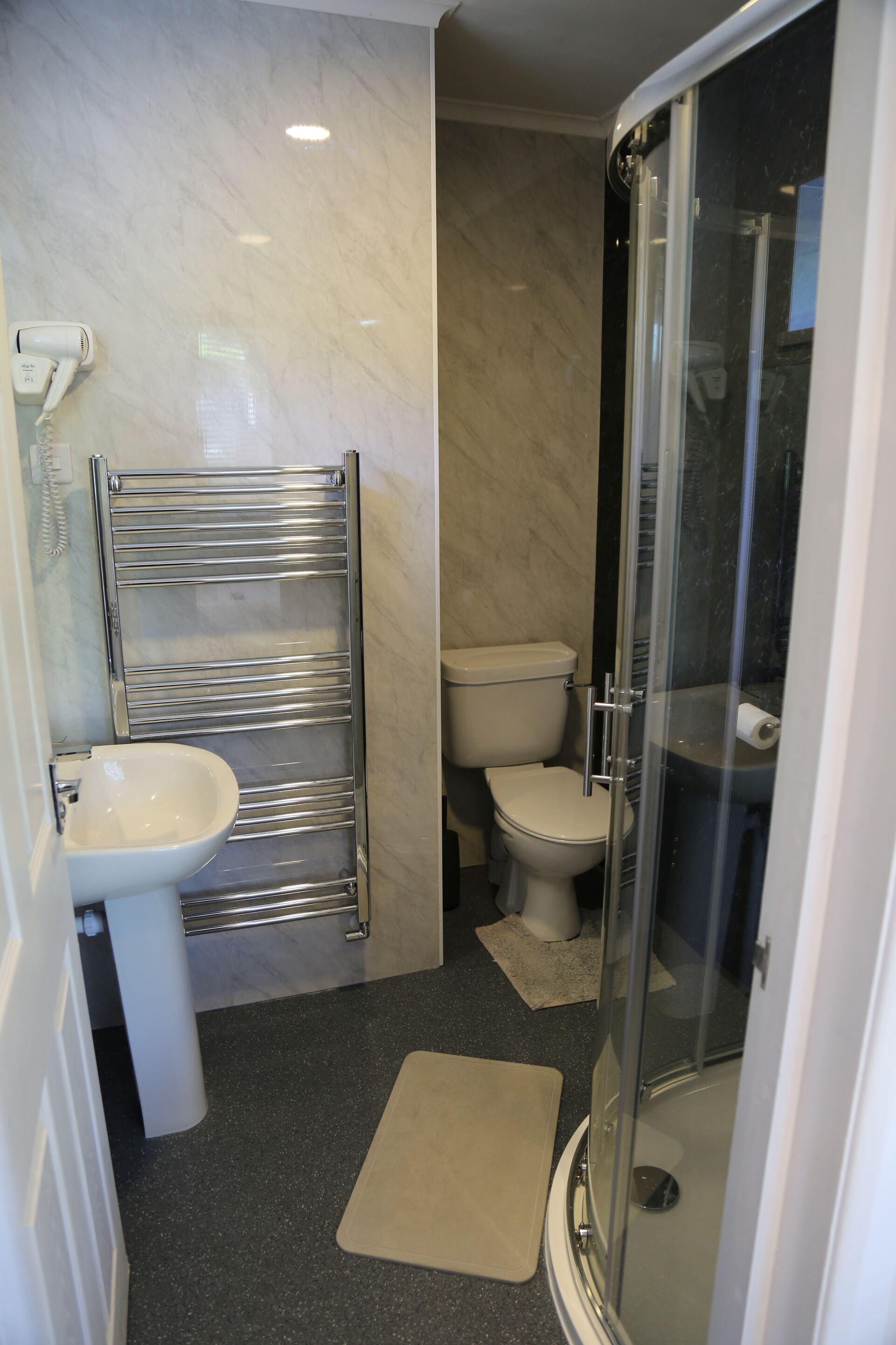 A modern bathroom with a glass shower enclosure, a white toilet, and a sink with a chrome towel rack.