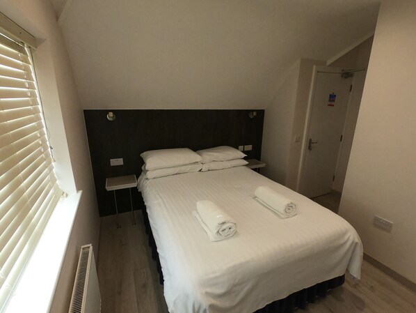 A hotel room with a single bed, a bedside table, a nightstand, and a window with blinds.
