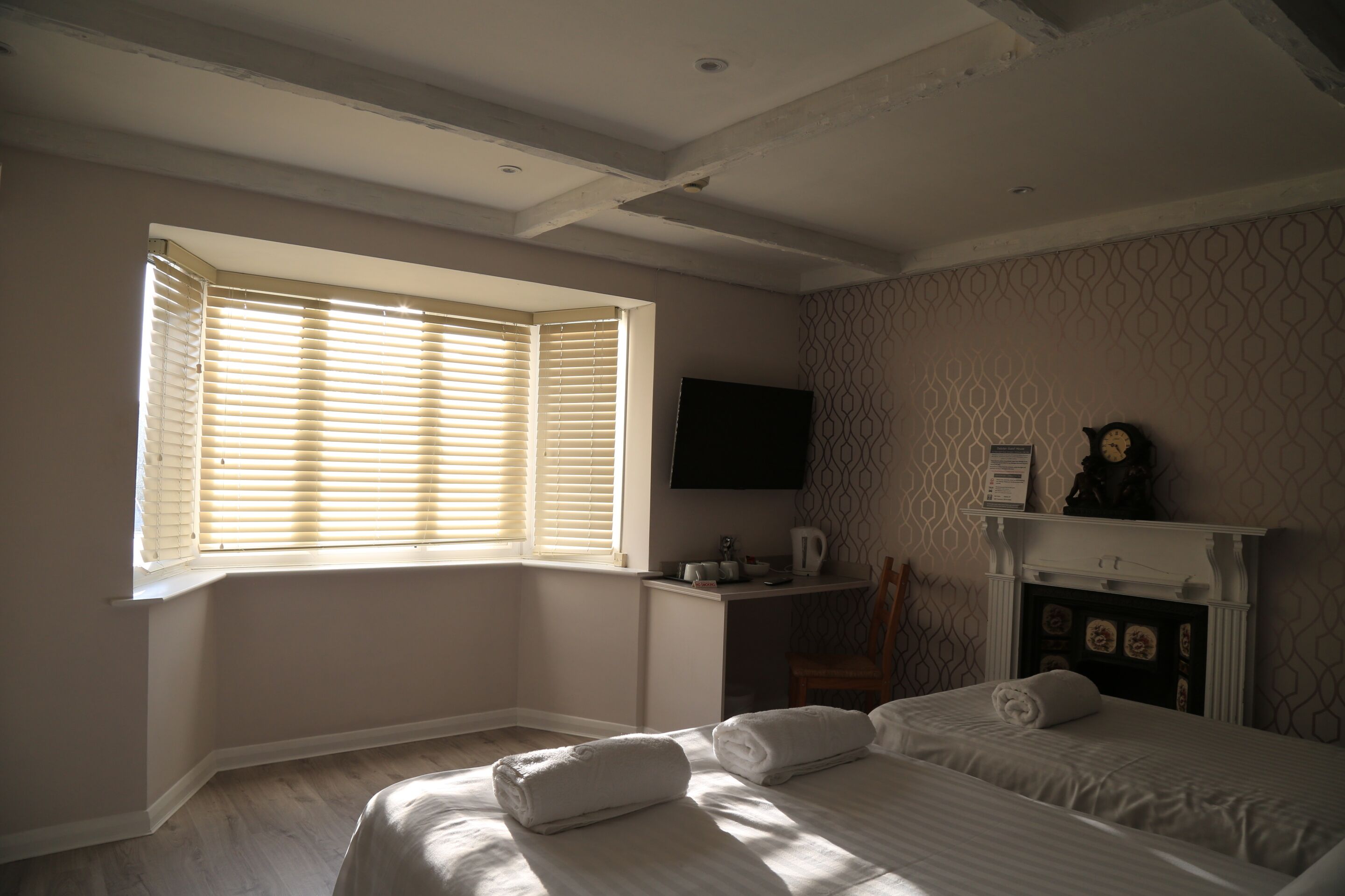 A bedroom with a bed, two towels, a desk with a chair, a flat-screen TV, and a fireplace.