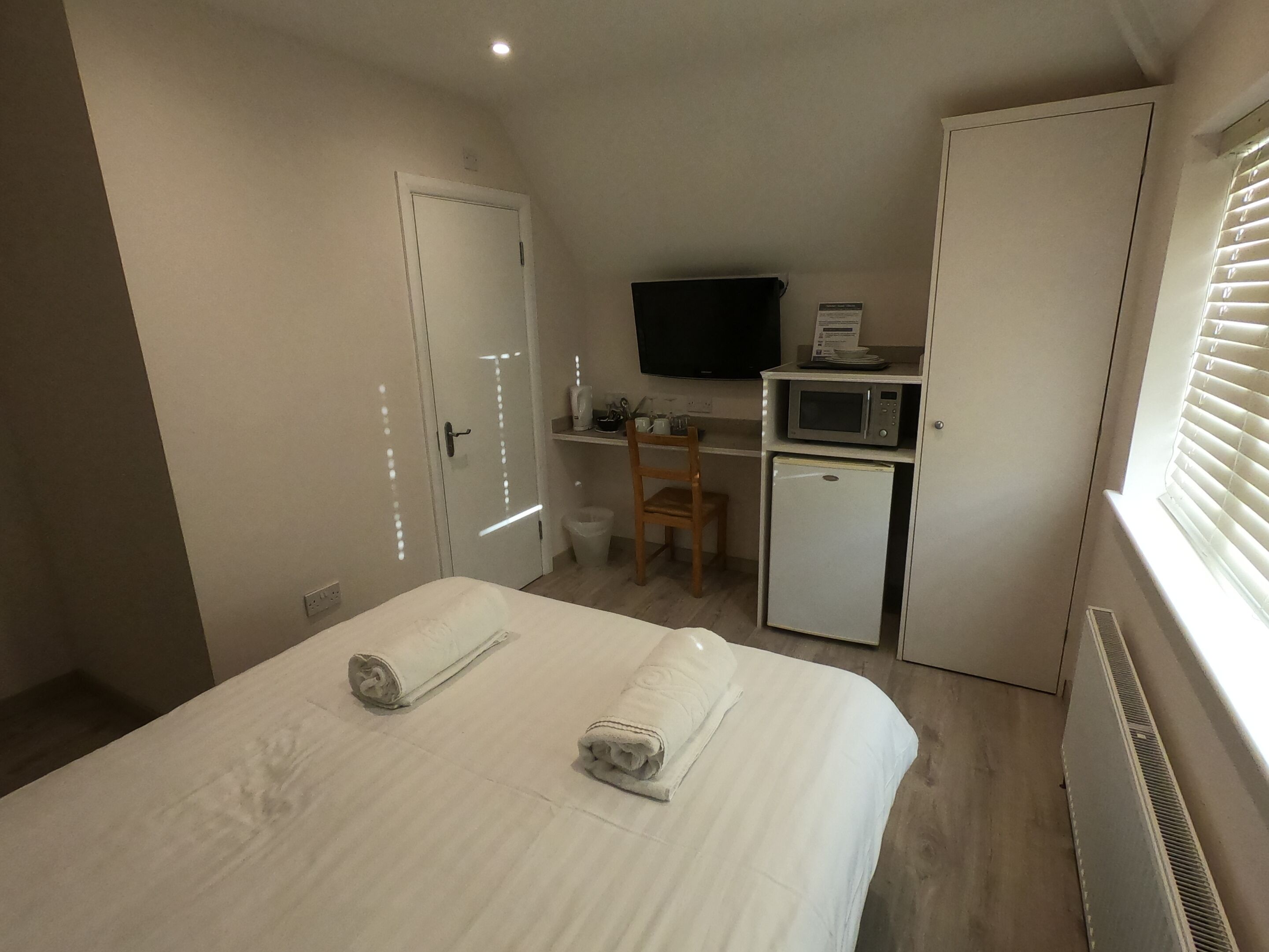 A small, compact room with a bed, a desk with a computer, a microwave, and a TV.